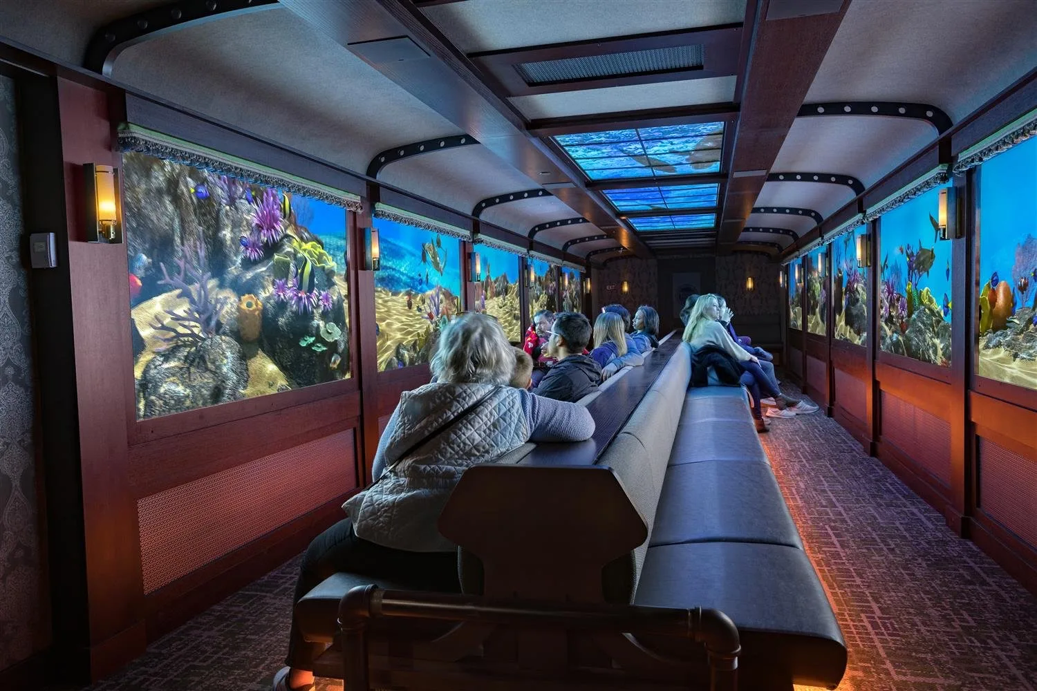 Guests seated in a train car with digital windows showing coral reef scenes at St. Louis Aquarium at Union Station