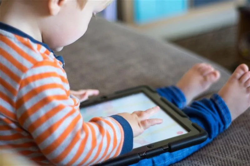 Toddler in a striped shirt tapping a tablet touchscreen