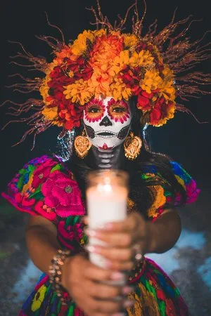 Woman in La Catrina face paint and marigold headdress holding a lit candle