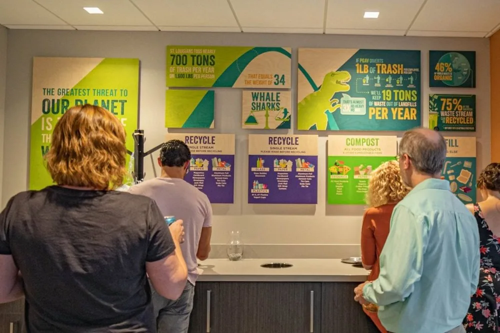 Visitors reading colorful recycling and compost signage above a waste station