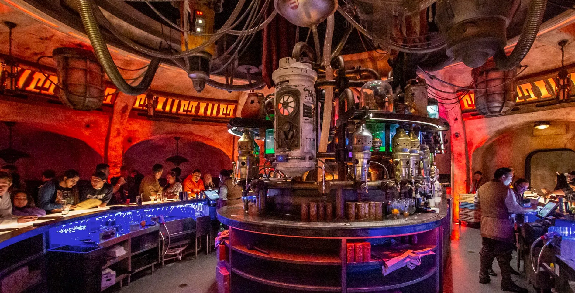 Guests at the bar beneath droid machinery in a dimly lit, Star Wars-themed cantina