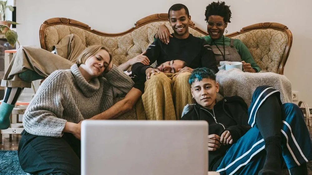 Diverse group of young friends relaxing together on a vintage sofa watching a laptop