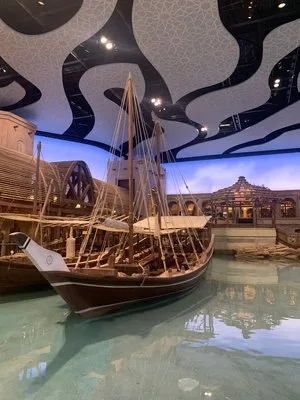 Traditional wooden dhow boat displayed in a shallow pool beneath a wave-patterned ceiling at SeaWorld Abu Dhabi