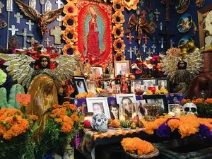 Dia de los Muertos altar filled with photos, marigolds, candles and an image of the Virgin of Guadalupe