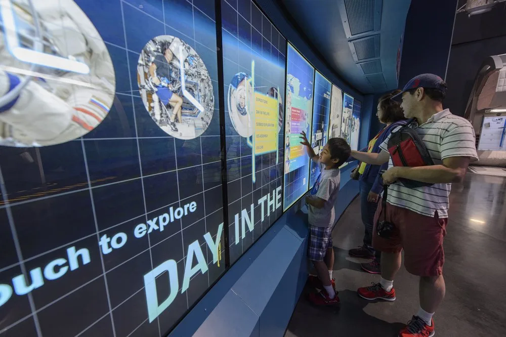 Family using a large touch-to-explore digital wall about a day in space at Kennedy Space Center Visitor Complex