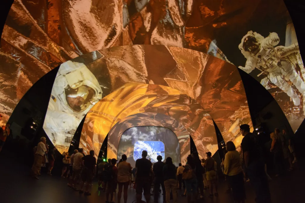 Visitors in a tunnel-like theater wrapped in projected astronaut and space imagery at Kennedy Space Center Visitor Complex
