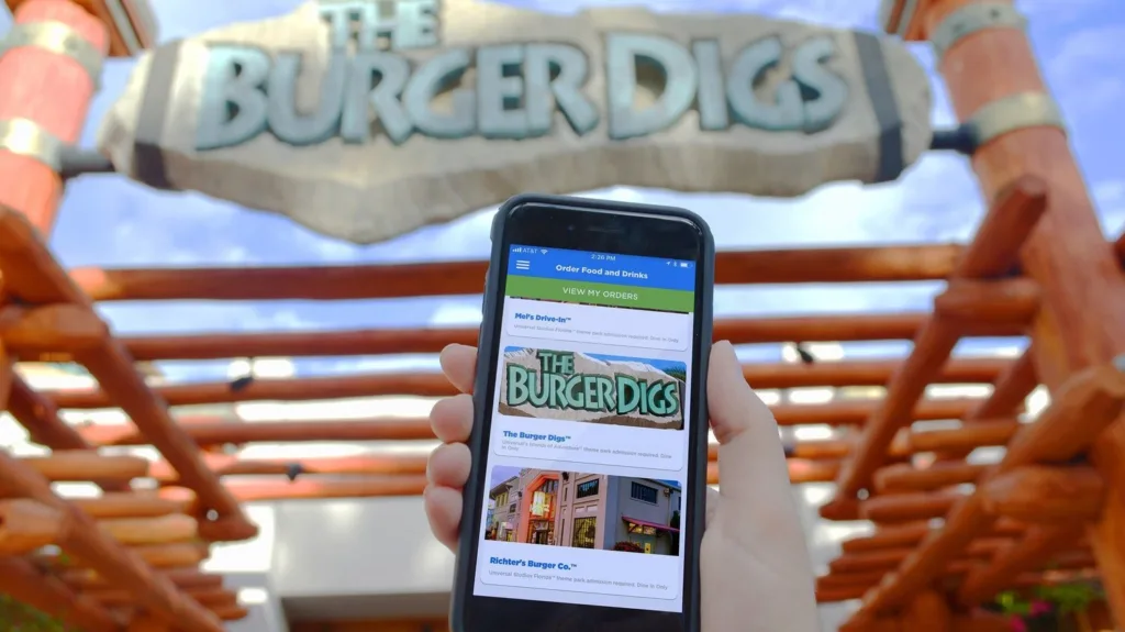 Phone showing the mobile ordering app in front of The Burger Digs restaurant sign at Universal