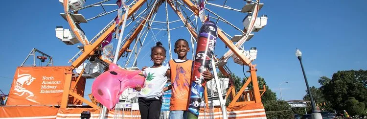 Kids smiling in front of a Ferris wheel on a fair midway
