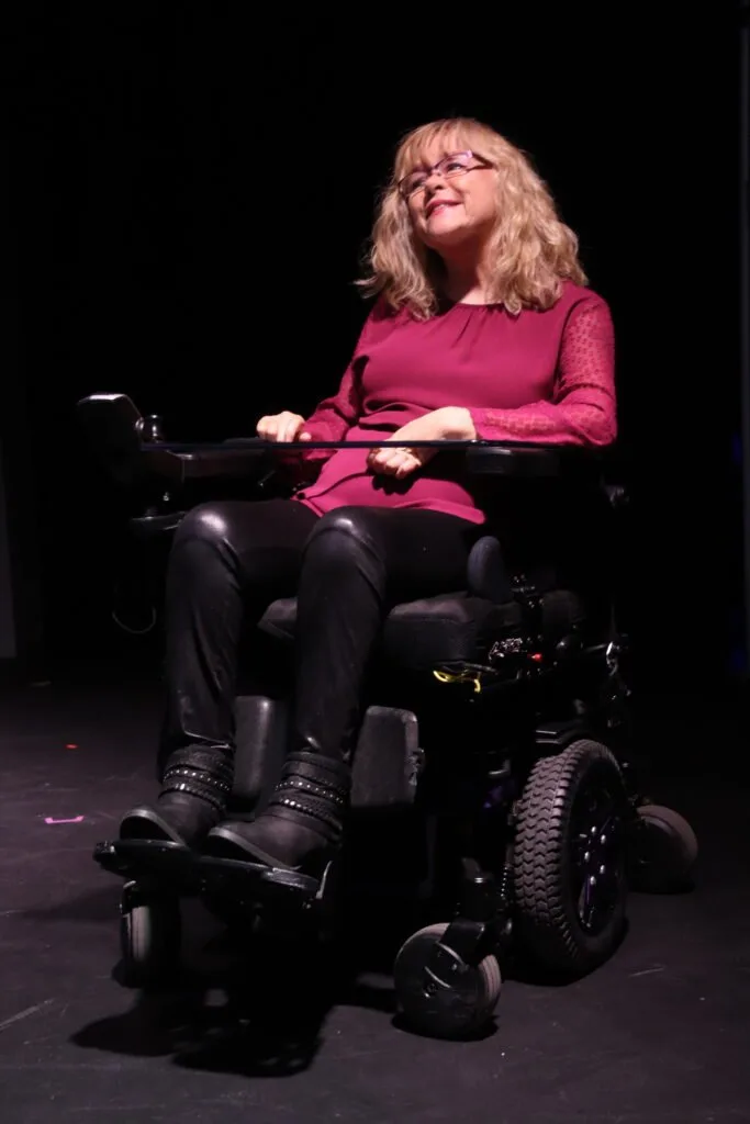 Katie Rodriguez Banister, founder of Access-4-All, in her power wheelchair on a darkened stage