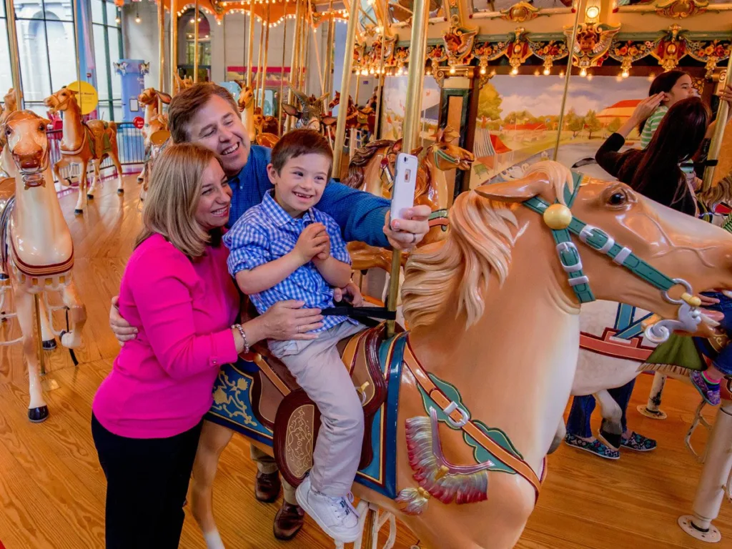 Family taking a selfie on the wheelchair-accessible vintage Dentzel carousel at Please Touch Museum