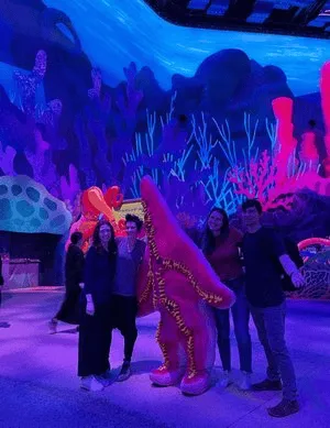 PGAV team posing with a costumed starfish character in a glowing coral-themed hall at SeaWorld Abu Dhabi