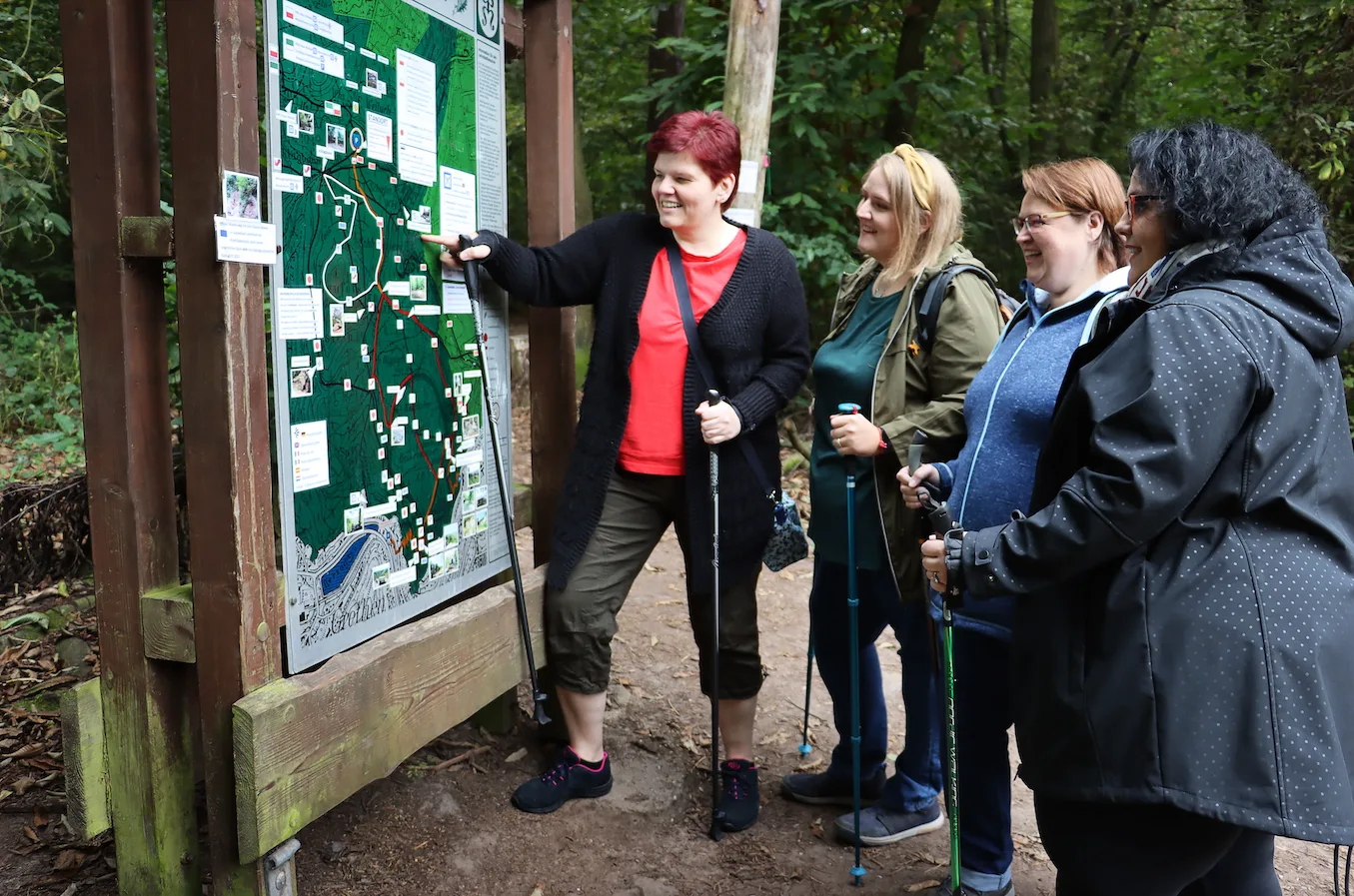 Group of plus-size women hikers with trekking poles studying a trail map at a trailhead