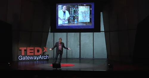 Speaker on stage at TEDxGatewayArch with a project image on the screen behind him