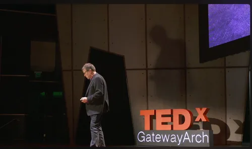 Speaker walking the stage beside the TEDxGatewayArch sign