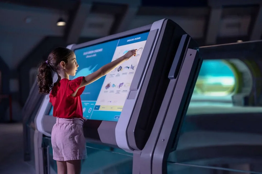 Girl using a large interactive touchscreen exhibit about ocean life at SeaWorld Abu Dhabi
