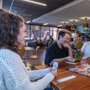 Friends laughing over a card game at a table in a bright social cafe