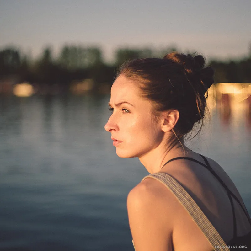Woman gazing thoughtfully across a lake at dusk