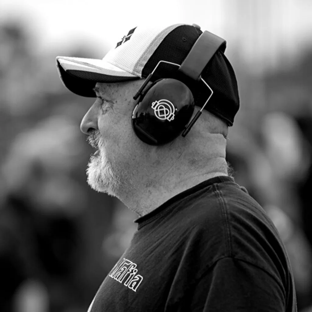 Man wearing KultureCity noise-reducing headphones at a crowded event, in black and white