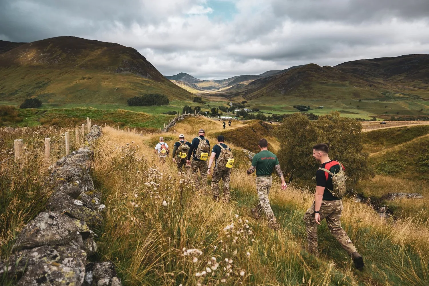Group of veterans hiking with packs through open hills and grassland