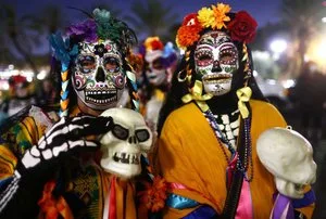 Two Dia de los Muertos celebrants in sugar skull makeup and flower crowns holding skulls