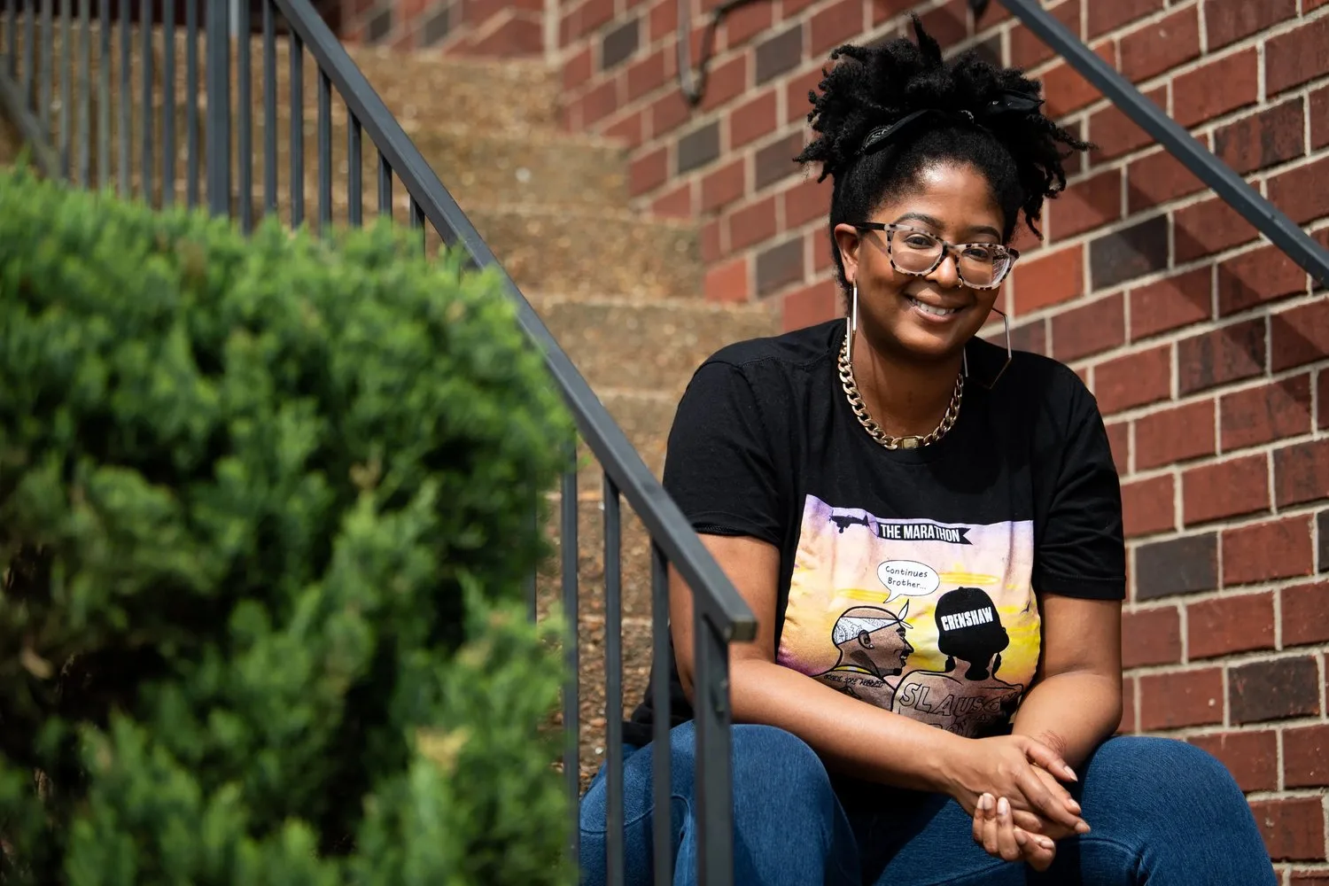 Smiling woman in glasses seated on brick steps beside a railing