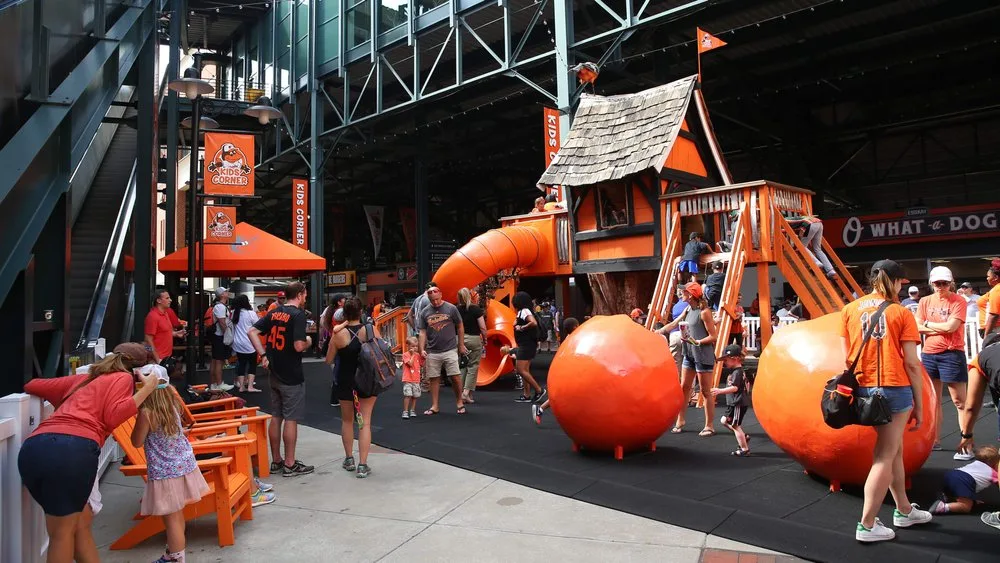 Families playing at an orange Orioles-themed treehouse play area inside the ballpark concourse