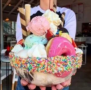 Oversized ice cream sundae piled with scoops, a donut and wafers in a sprinkle-rimmed bowl