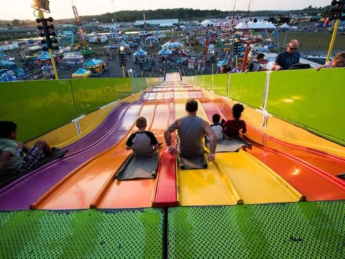 Families riding sacks down a giant rainbow-colored slide at a state fair