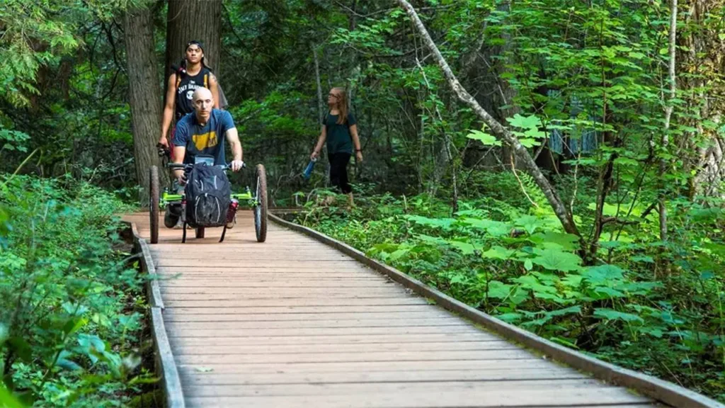 Visitor using an off-road wheelchair on an accessible boardwalk trail through a national park forest