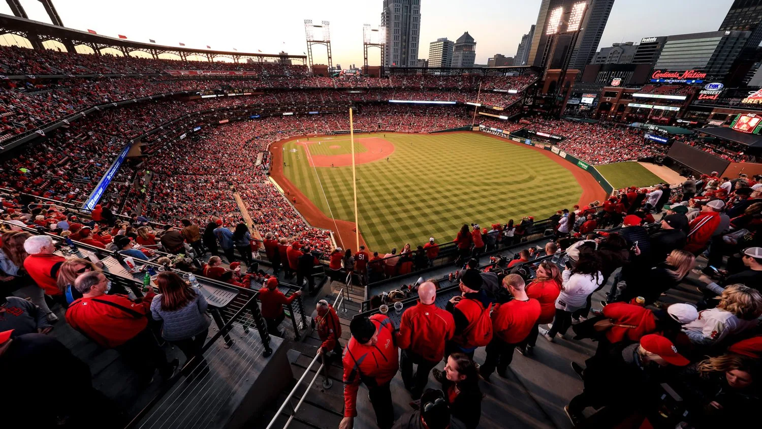 Packed crowd in red watching a Cardinals game at Busch Stadium from an upper deck at dusk
