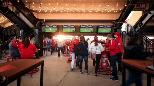 Fans in Cardinals red gathering at a bar concourse with game screens at Busch Stadium