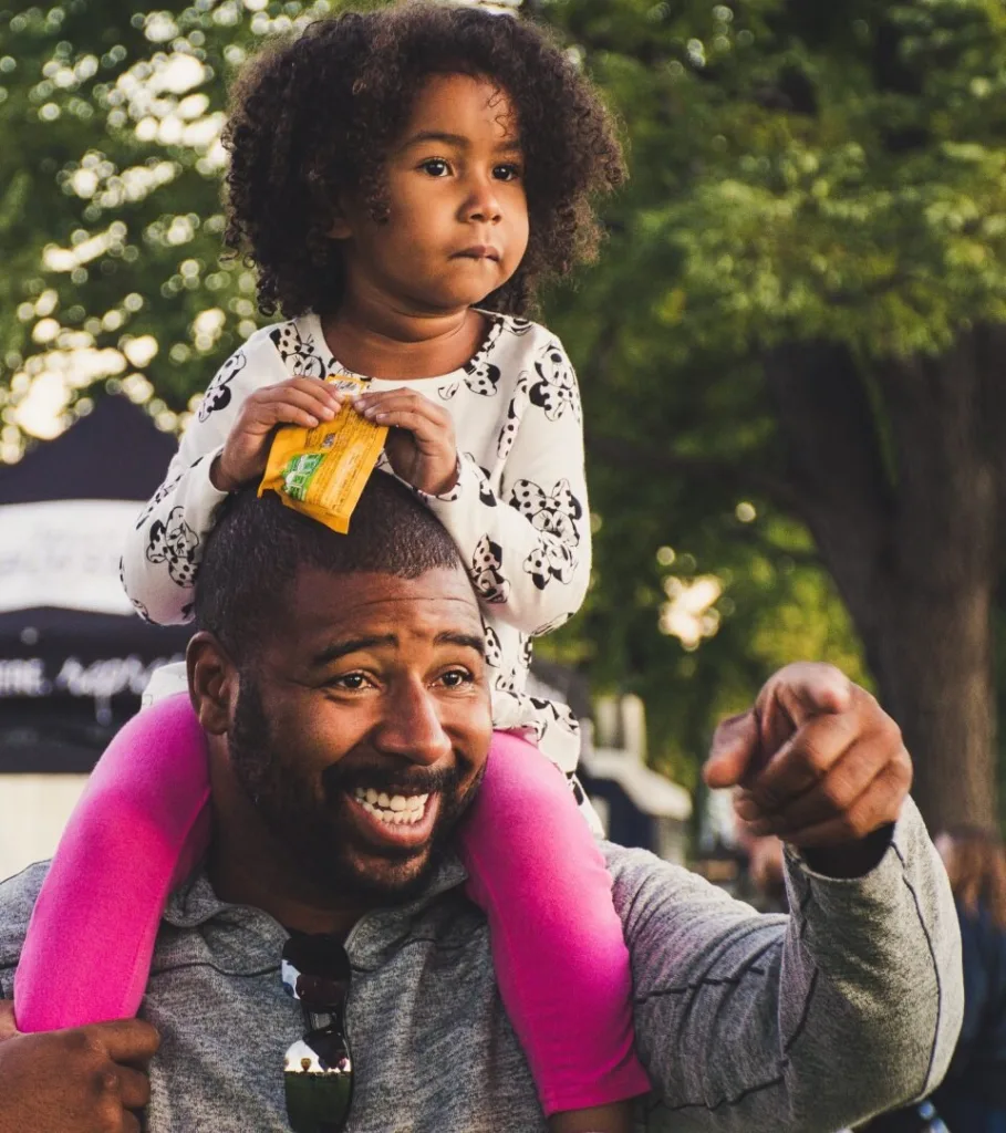 Smiling father carrying his young daughter on his shoulders at an outdoor event