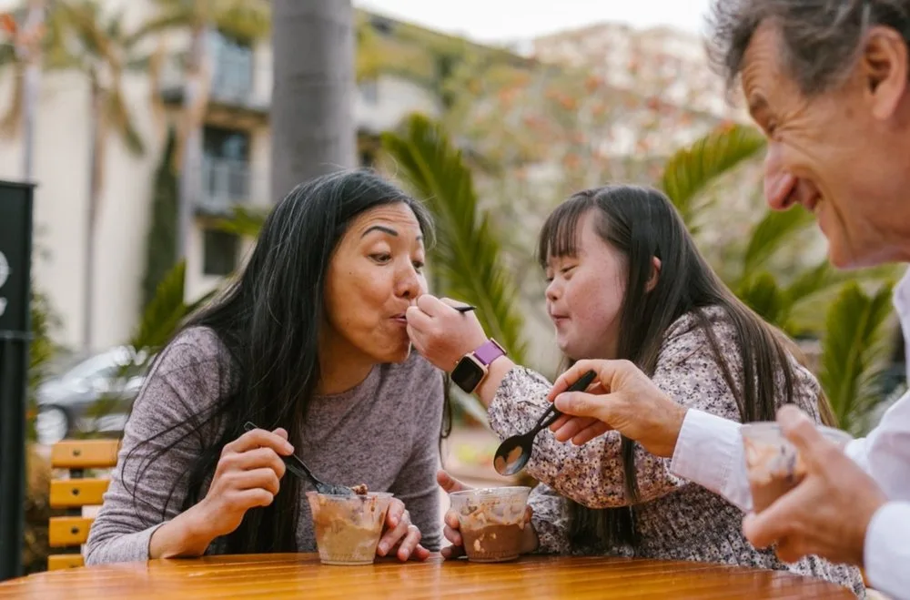 Mother, grandfather and a girl with Down syndrome sharing ice cream at an outdoor café table