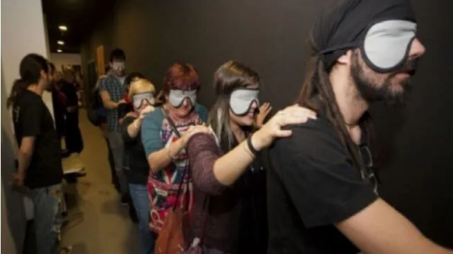 Blindfolded audience members guided single file through a dark corridor at Teatro Ciego