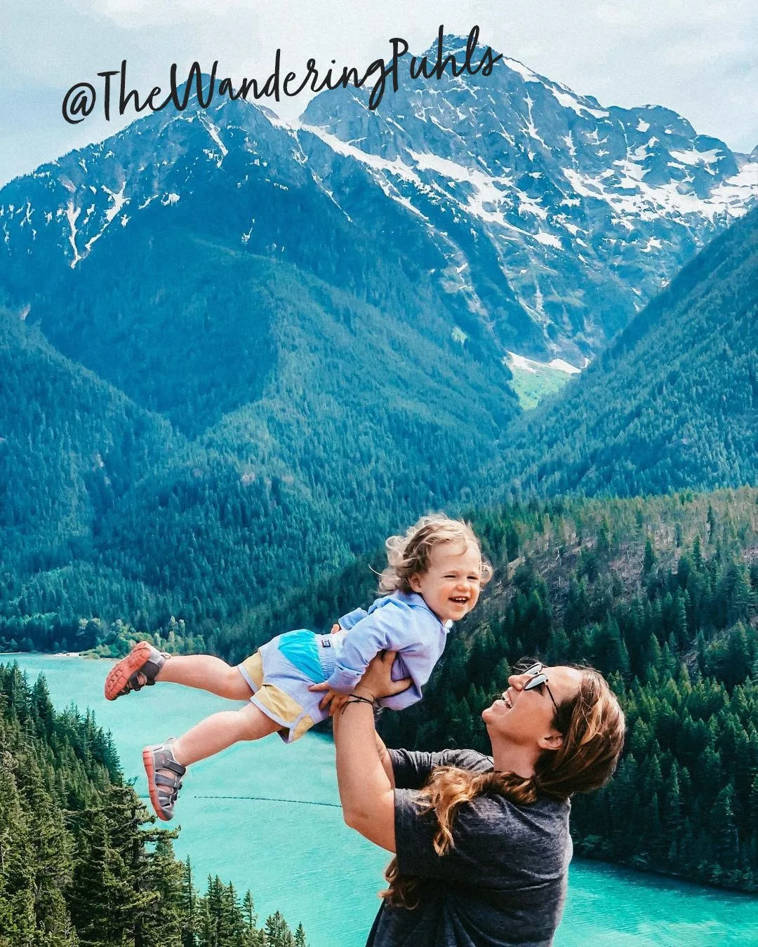 Mother lifting her toddler above turquoise Diablo Lake in the mountains, posted by @TheWanderingPuhls