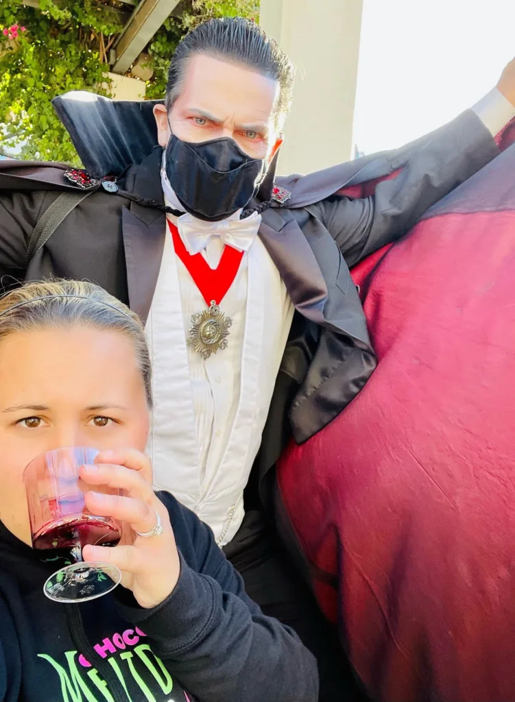 Guest sipping a drink in a selfie with a masked Dracula character at a theme park