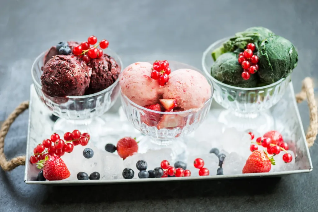Three bowls of vegan nice cream in berry, strawberry and spinach flavors topped with fresh berries on ice