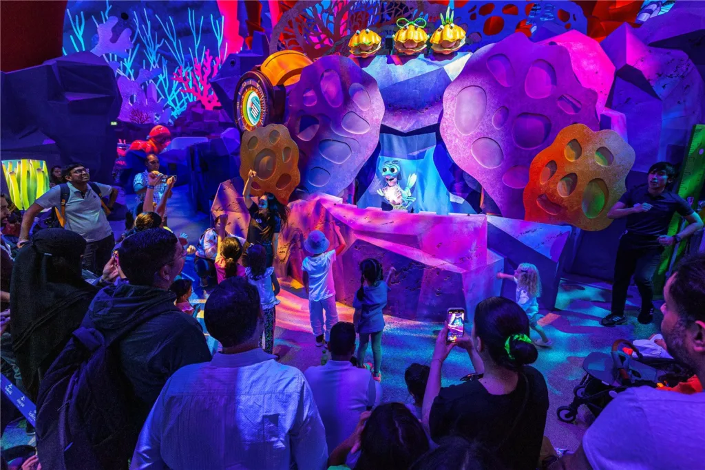 Families watching a character show in a glowing, candy-colored themed play space