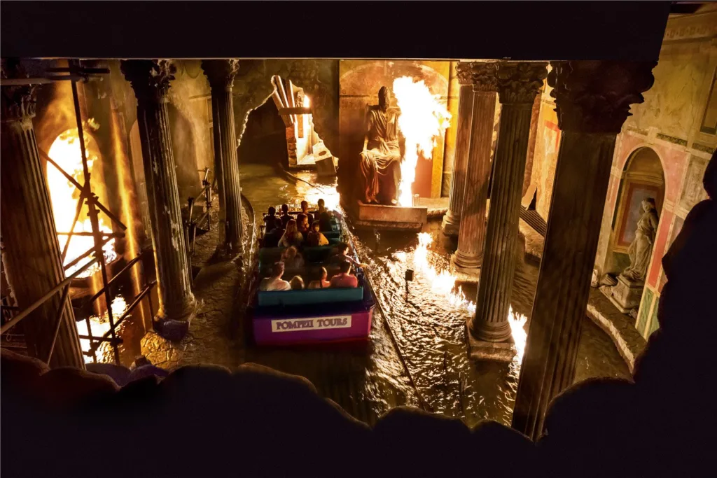 Boat of riders passing flaming Roman columns on the Escape from Pompeii water ride