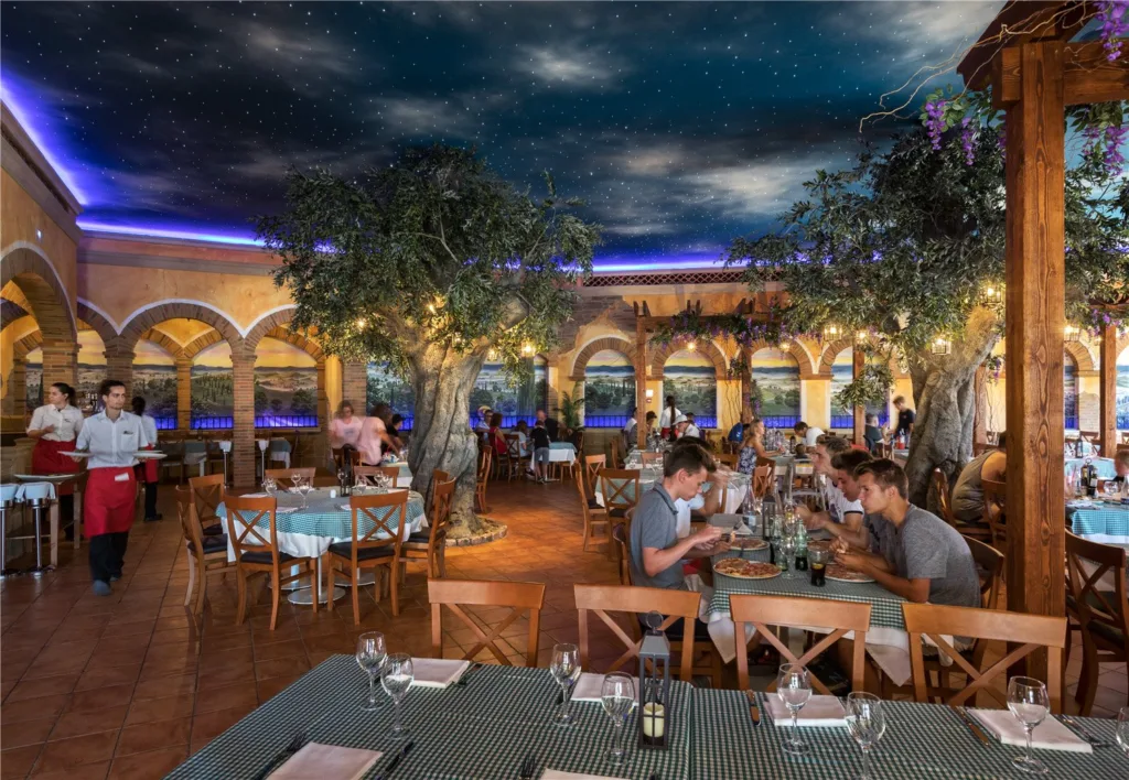 Guests dining in an Italian courtyard-themed restaurant with olive trees under a starry ceiling