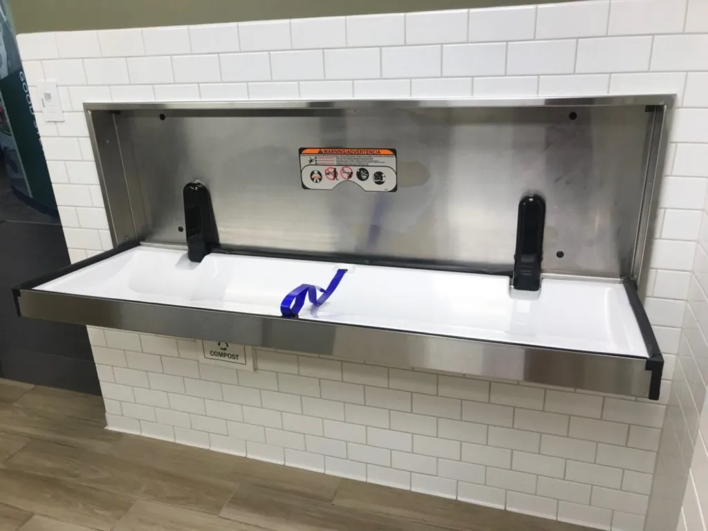 Wall-mounted stainless steel adult changing table in a tiled accessible restroom