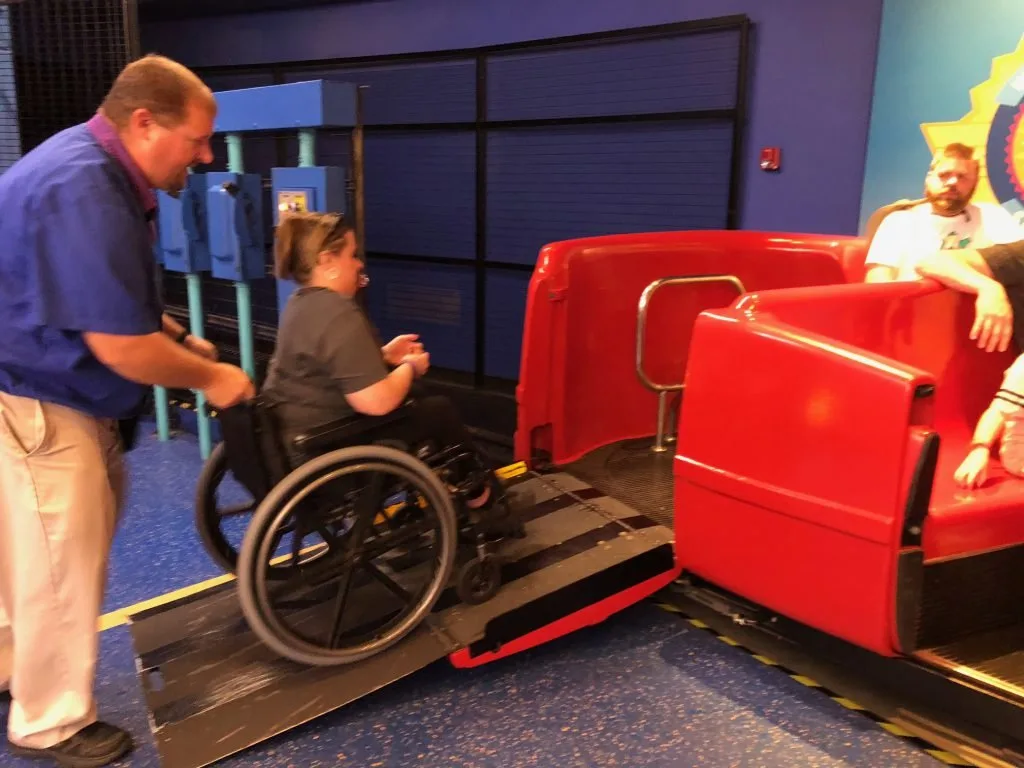 Staff member helping a guest in a wheelchair roll up a ramp to board a ride vehicle