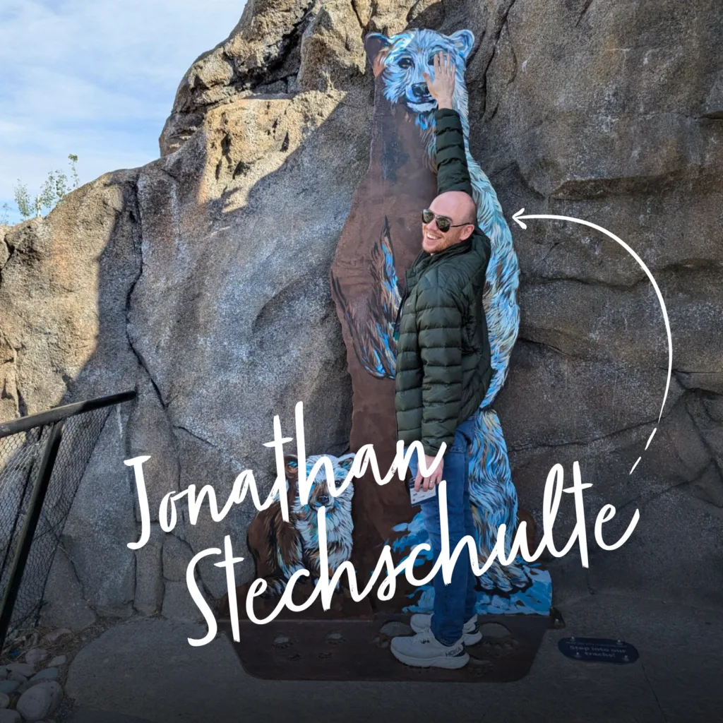 Jonathan Stechschulte posing beside a carved bear sculpture on a rockwork wall