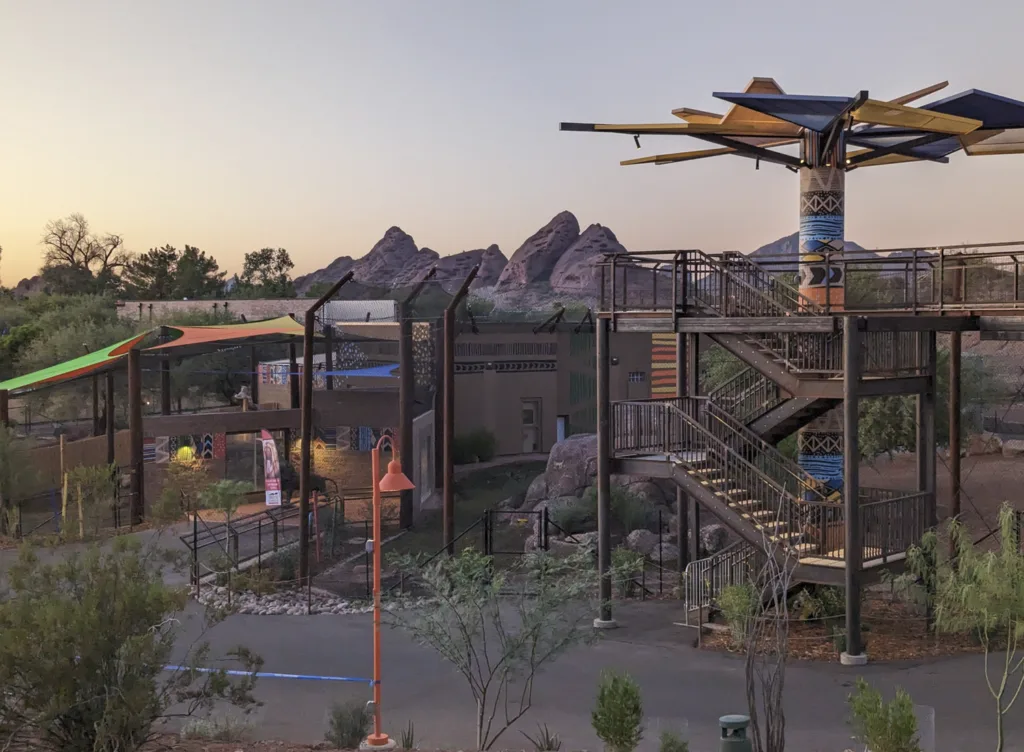 Predator Passage at the Phoenix Zoo at dusk, with a stair tower, shade canopies and desert buttes beyond