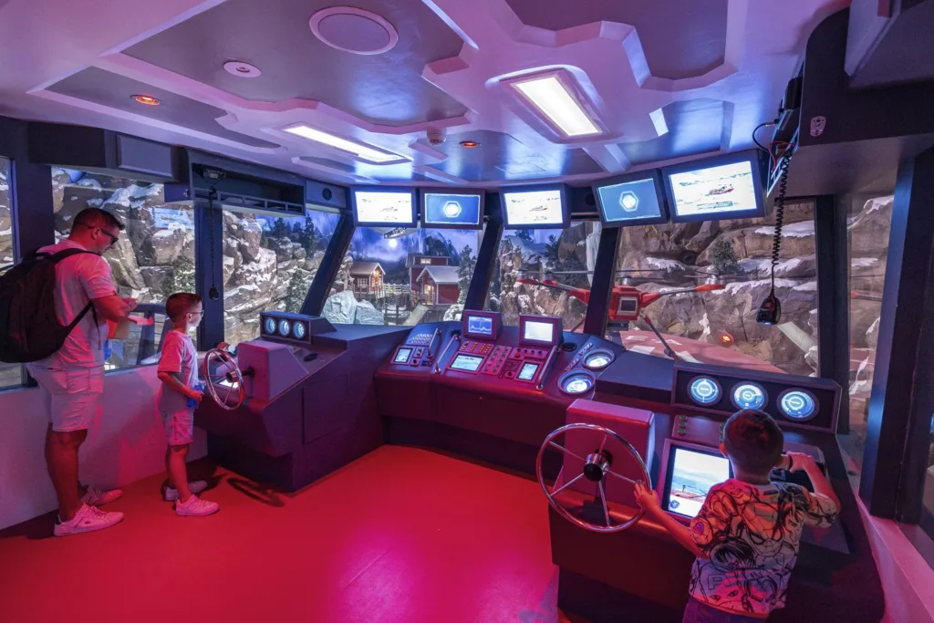 Children steering at the controls of a ship bridge simulator overlooking a polar model landscape