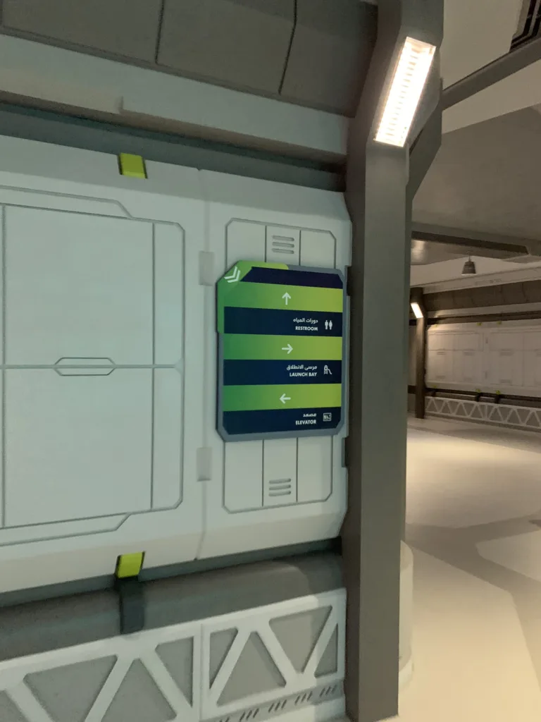 Green and navy wall-mounted directional sign in a spaceship-style corridor in the Endless Ocean realm at SeaWorld Abu Dhabi