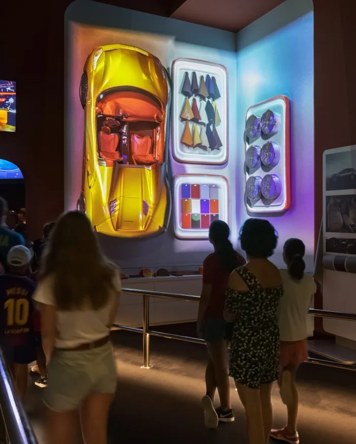 Guests viewing a glowing display of a yellow Ferrari and car parts in the Ferrari Experience at Ferrari Land, PortAventura