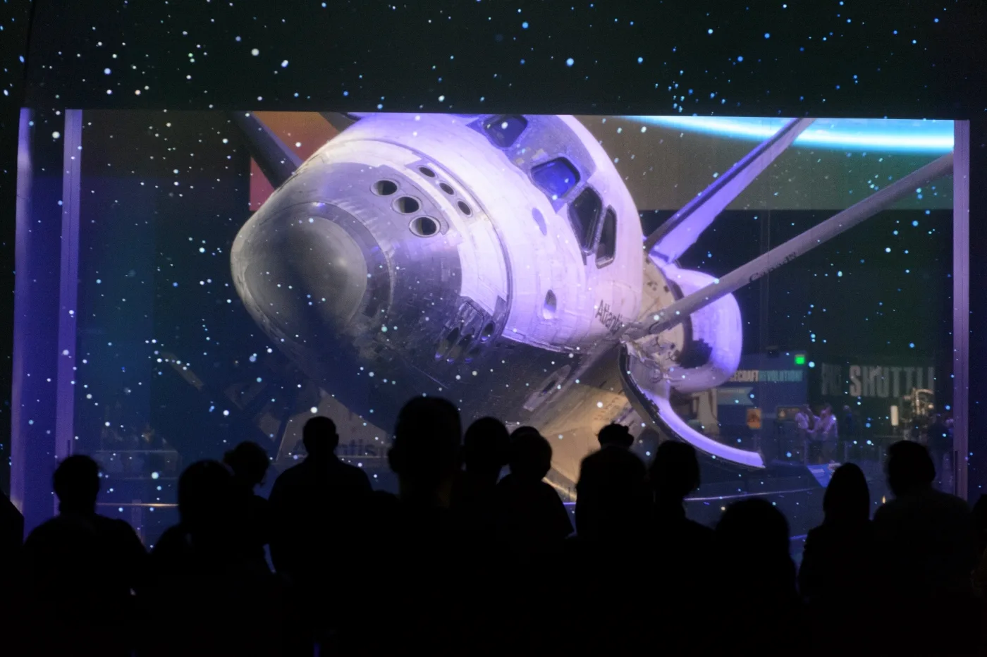 Visitors silhouetted during the reveal of Space Shuttle Atlantis against a starfield at Kennedy Space Center Visitor Complex