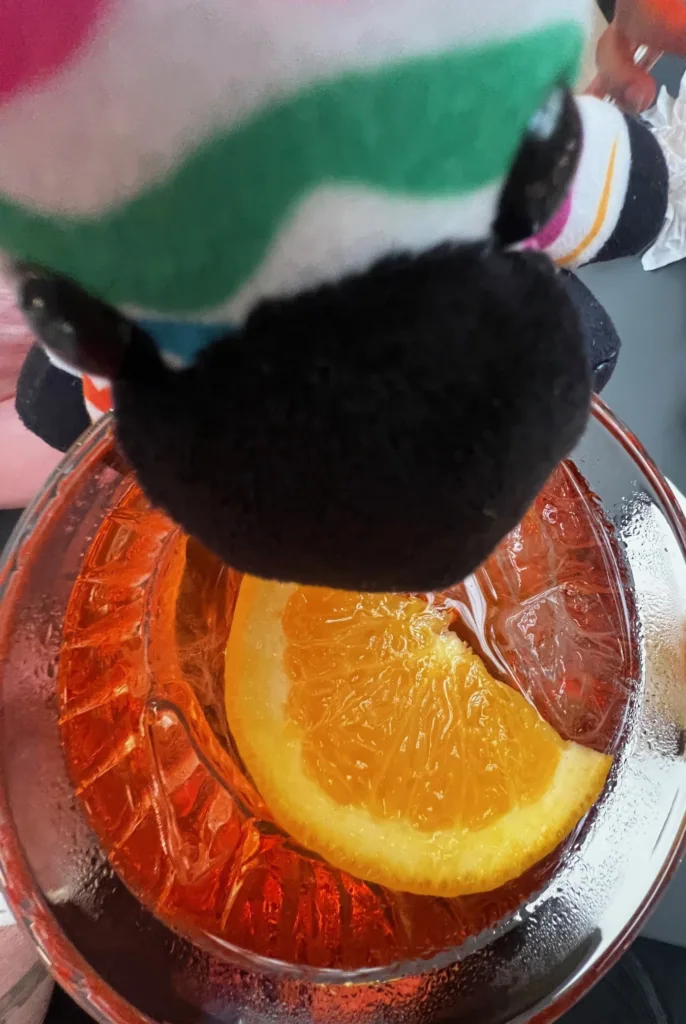 Spot, PGAV's zebra plush mascot, peering into a spritz cocktail with an orange slice