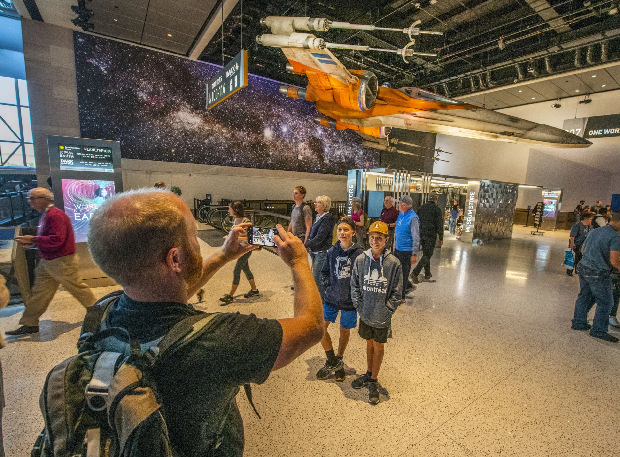 Father photographing his sons beneath a Star Wars X-wing fighter at the Smithsonian National Air and Space Museum